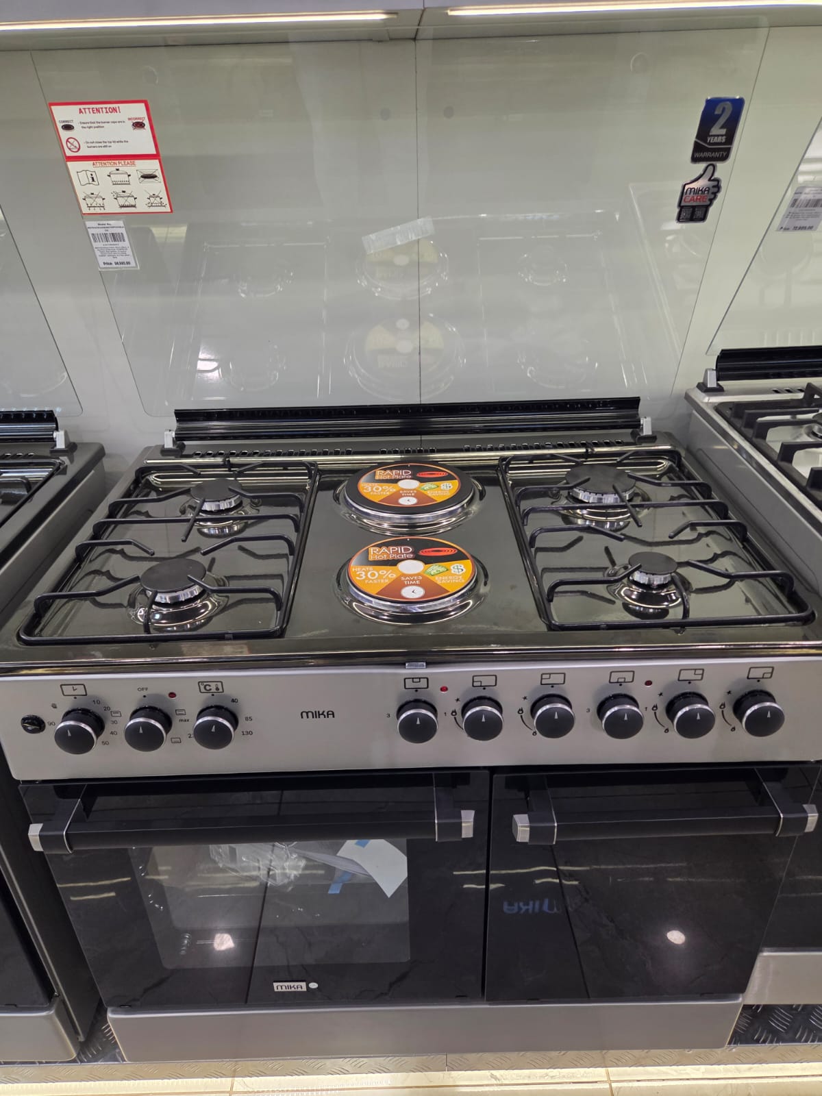 Mika Standing Cooker, 90cm X 60cm, 4 Gas Pool Jet Burners + 2 RAPID Hot Plates, Auto Ignition, Flame Failure Safety,4 Function Electric Oven, Gas Cylinder Cabinet, Rotisserie, S.S Hob, Silver Body.